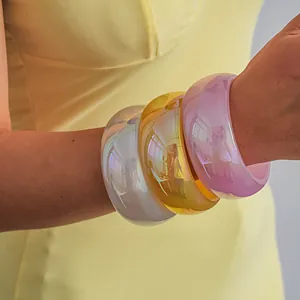 Macro detail showing colorful iridescent resin bangles on a wrist with dopamine style colors