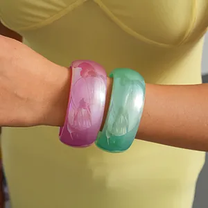 Detail shot of vibrant pink and green resin bangles worn on a wrist.