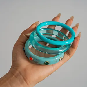 Detail view of a three-piece turquoise resin bangle set with colorful rhinestones in hand.