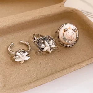Détail de bagues bohèmes en coquillage et étoile de mer avec perles sur plateau.