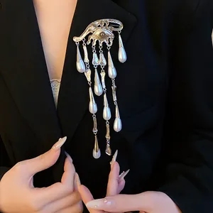 Detailed view of eye-shaped brooch with pearl teardrop tassels on a black blazer