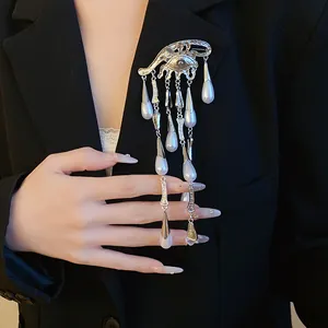 Close-up of silver eye-shaped brooch with pearl waterdrop tassels on black blazer.