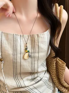 Close-up view of forest style plant acorn necklace worn by model in linen striped dress