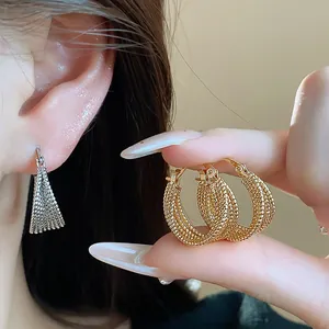 Detail of 18k real gold plated textured hoop earrings held by manicured fingers.