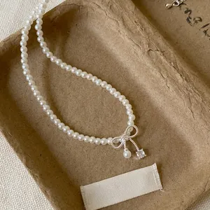 Close-up of an elegant pearl necklace with a zircon bow pendant on a textured tray