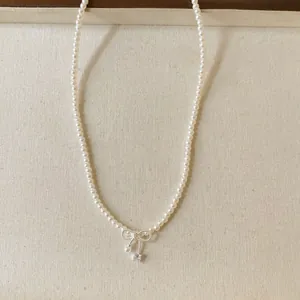 Close-up detail of pearl necklace with bow-shaped zircon pendant and soft textile backdrop