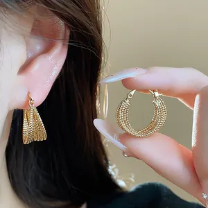 Detailed macro shot of textured 18k gold plated hoop earrings shown on ear and held by hand