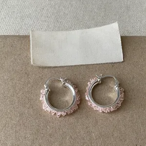Nahaufnahme eleganter silberner Creolen, verziert mit funkelnden rosa Glasscherben