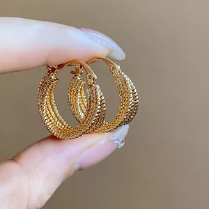 Close-up detail of 18k gold plated textured mesh hoop earrings held between fingers.