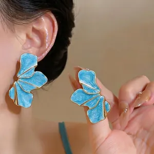 Elegant blue oil-drop petal earrings with metallic gold trim shown on model's ear