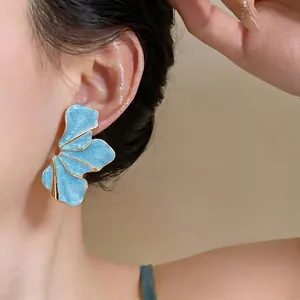 Close-up showing the intricate texture of blue enamel petal earrings with gold trim