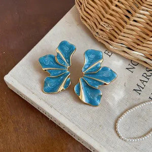 Elegant blue enamel petal stud earrings with gold edges shown on vintage book detail.