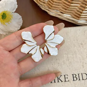 Close-up of white enamel petal ear studs with gold-plated edges and artistic texture