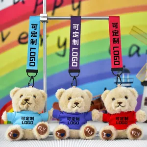 Close-up of three plush teddy bear keychains with colorful shirts on a display stand
