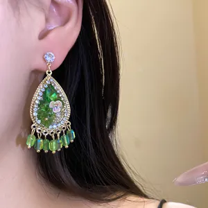 Detail van bohemien druppelvormige kwastjes oorbellen met groene hars en strassteentjes.