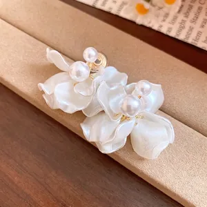 Elegant white flower petal earrings with lustrous pearls shown on a brown display stand