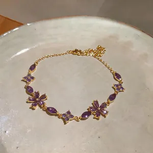 Macro detail of elegant purple zircon flower charms on a minimalist gold-plated bracelet
