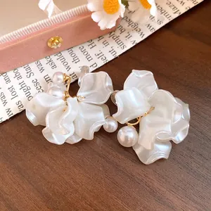 Detail view of elegant white petal earrings with pearl accents on a wooden background