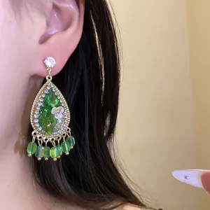 Close-up van bohemian groene hars druppeloorbellen met bloemaccenten en kwastjes.