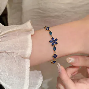 Close-up of a French style gold bracelet featuring blue zircon flower charms on wrist