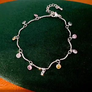 Close-up of multi-colored circular zircon charms on a silver necklace over green velvet