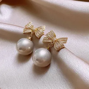 Detailed close-up view of elegant gold-toned zircon bow earrings with large lustrous drop pearls