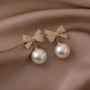Macro detail of elegant gold bow earrings featuring pavé zircons and dangling white pearls