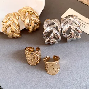 Close-up of gold and silver chunky braided C-shaped hoop earrings and textured rings.
