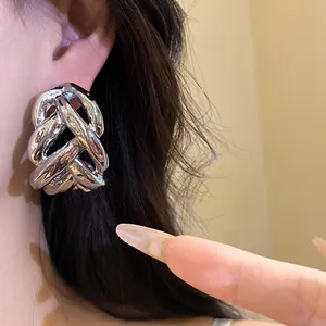 Macro view showing the intricate knot design of oversized silver metal C-shaped earrings