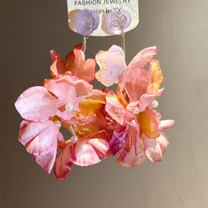 Dettaglio di orecchini a fiore in tessuto rosa con perle e rose in resina viola