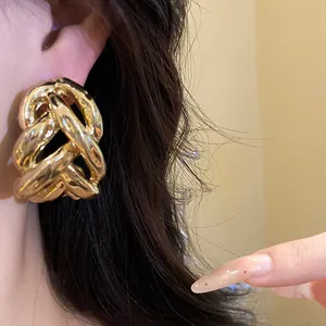 Close-up of chunky gold intertwined knot stud earrings showing detailed metal texture