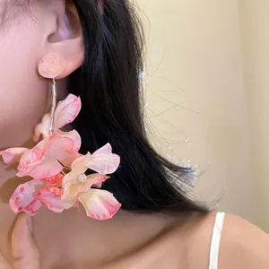 Dettaglio ravvicinato di orecchini floreali in tessuto rosa con perle su una modella