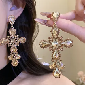 Primo piano di orecchini a croce in cristallo champagne con eleganti pendenti a goccia.