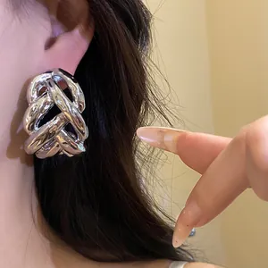 Close-up detail of chunky silver-toned twisted knot stud earrings with a high-shine finish