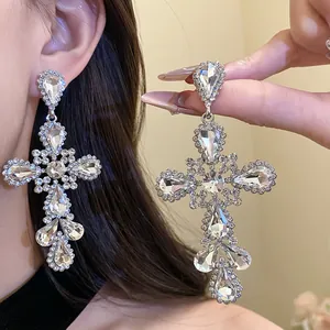 Dettaglio macro di orecchini a croce in argento con brillanti strass a goccia