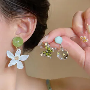 Dettaglio di orecchini a forma di farfalla e fiore con cristalli e sfere di vetro decorato.