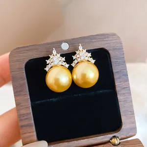 Detail shot of elegant golden pearl earrings with crown-shaped zircon embellishment