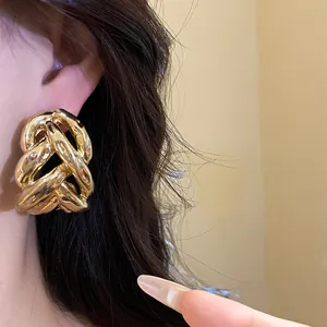 Detail view of chunky gold metallic knot stud earrings with a high-polished mirror finish