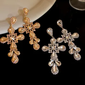 Dettaglio di lussuosi orecchini a croce con pendenti a goccia di cristallo scintillante.