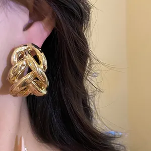 Macro view of chunky gold-colored intertwined chain-link statement stud earrings on ear.