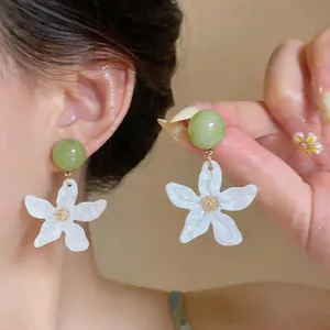 Primo piano di eleganti orecchini con perla verde e fiore bianco con finitura perlata.