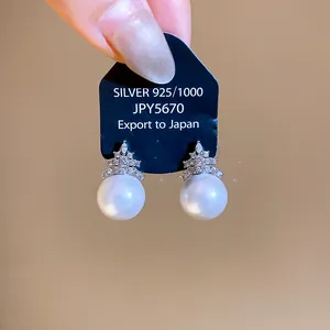 Detail view of shimmering zircon and pearl stud earrings with a silver geometric base