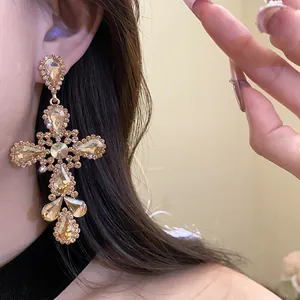 Dettaglio di orecchini pendenti a croce dorata con strass scintillanti e ciondoli a goccia