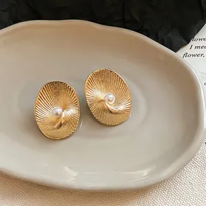 Macro view of gold oval earrings with textured radial pattern and central pearl