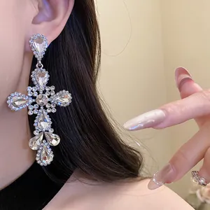 Dettaglio di orecchini pendenti a croce con strass e pendenti a goccia d'acqua su modella.