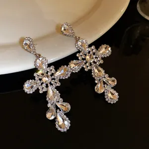 Vista macro di orecchini ad ago in argento con design a croce di strass e goccia