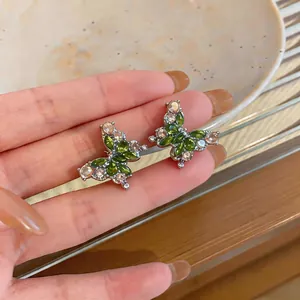 Primo piano di eleganti orecchini a farfalla con intarsi di cristalli verdi e rosa