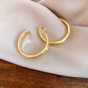 Dettaglio di eleganti orecchini a cerchio a C in oro opaco su morbida seta rosa