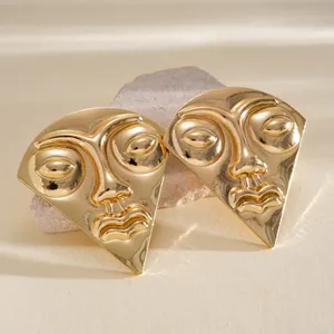 Elegant gold abstract face earrings with detailed facial features displayed on a stone prop