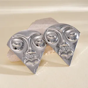 Macro detailed view of artistic silver face mask stud earrings with a polished mirror finish.